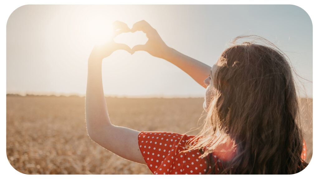 Girl with a heart shape fingers at sunlight