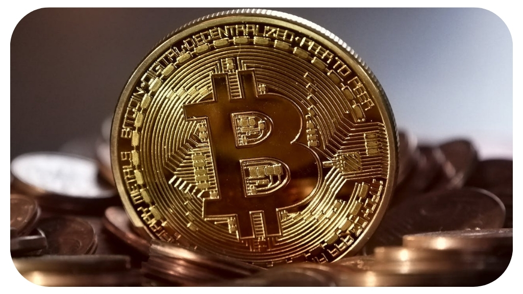 Close-up of a shiny gold Bitcoin coin standing upright among a pile of other coins.