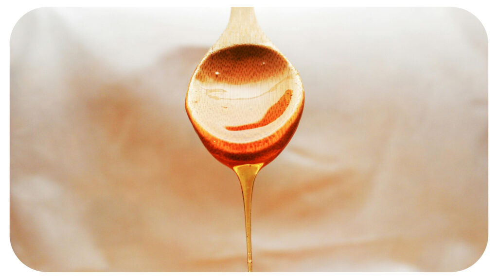 A wooden spoon drips golden honey against a soft, warm background—highlighting its natural, rich texture and purity.