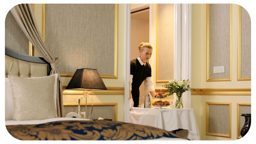 A hotel staff member carefully setting a breakfast tray with pastries, coffee, and flowers inside a luxurious suite with elegant gold-trimmed walls and soft lighting, representing the refined guest experience and attention to detail that define a five-star brand.