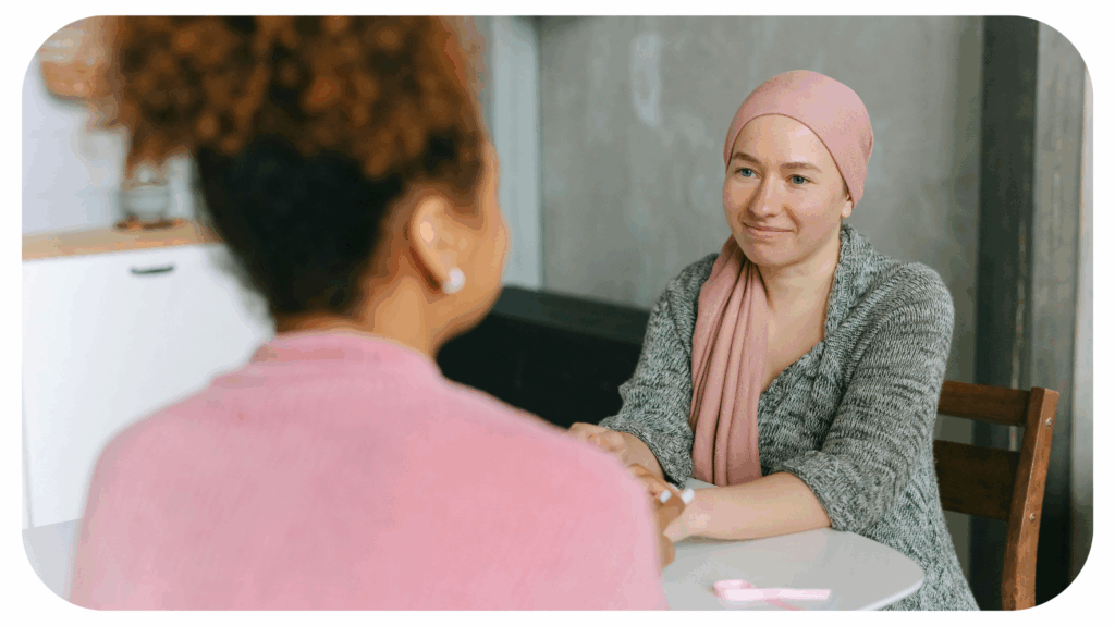 A woman holding hands with a cancer patient wearing a pink headscarf, symbolising emotional support, care, and empathy for those undergoing cancer treatment.