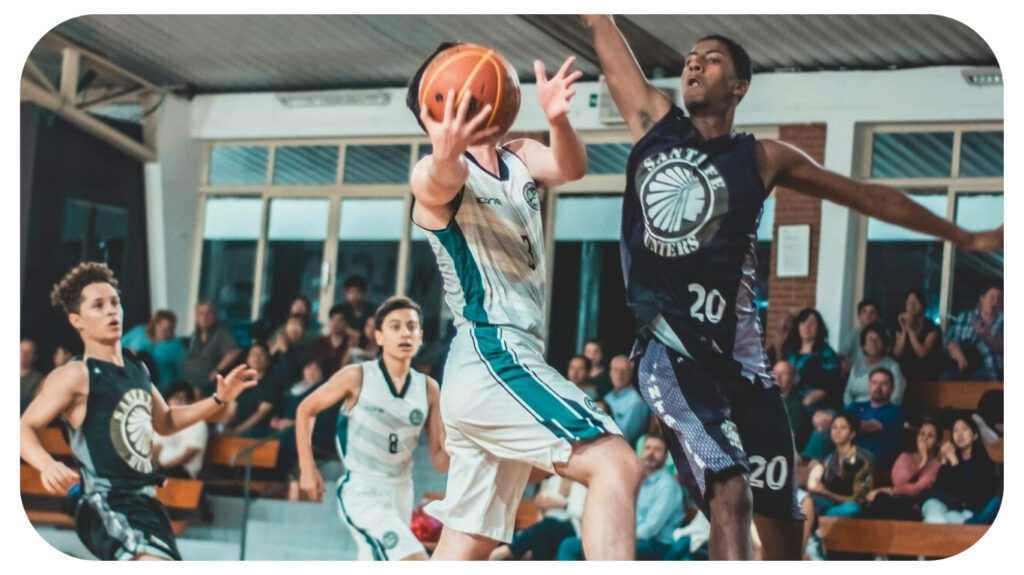 High school basketball players in action during a fast-paced game, with one player driving toward the basket while others defend, highlighting school athletics and the importance of gymnasium facilities.