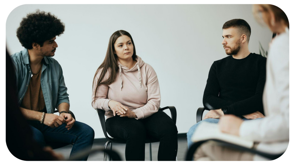 Female attender of group therapy sharing her issues with a therapist and other participants during their meeting at community center.