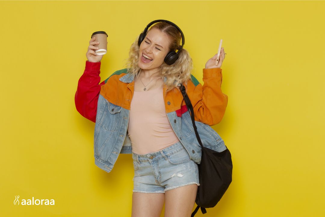 Young woman enjoying music with headphones while holding coffee and phone against a bright yellow background, representing modern lifestyle, self confidence and everyday fashion inspiration for women on MostInside.