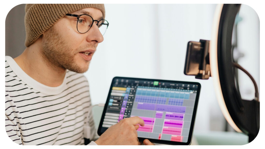 Music producer using digital audio workstation software on a tablet during online music production setup with recording equipment and audio editing tools.