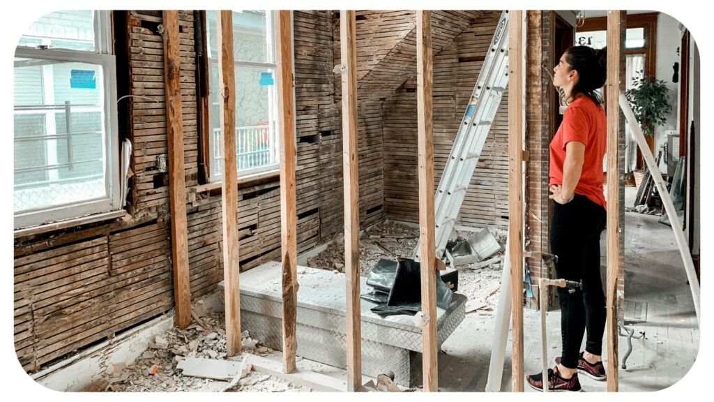 Homeowner inspecting an active home renovation project with exposed framing and construction materials while planning and organizing a remodeling project to stay on schedule and within budget.