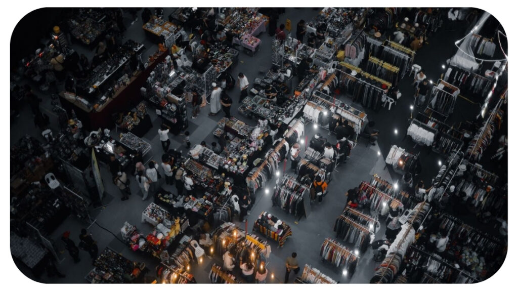 Aerial view of a busy indoor market with vendor stalls, clothing racks, and shoppers browsing.
