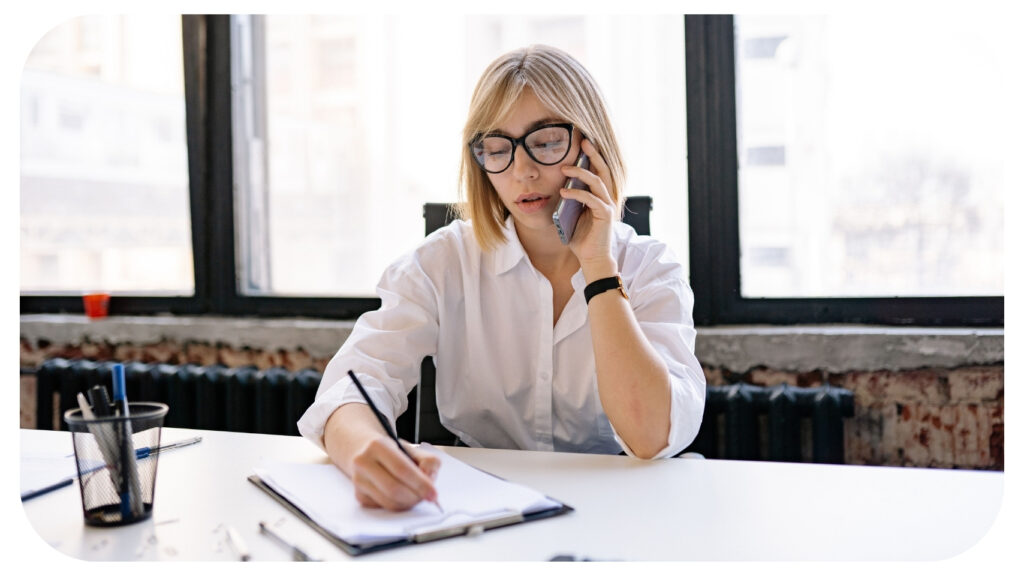 Business professional taking notes during a client call, illustrating effective workplace communication, cross-functional collaboration, knowledge sharing, team coordination, and strategies to break down communication silos for a more connected and productive organization.
