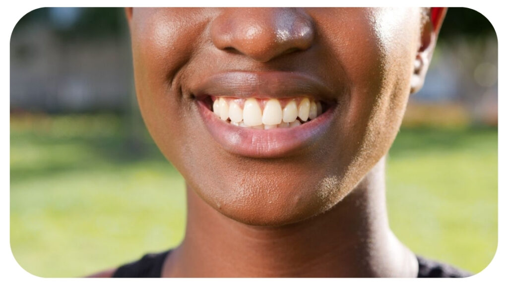 Close up of a woman's smiling mouth showing a full, healthy set of teeth outdoors.